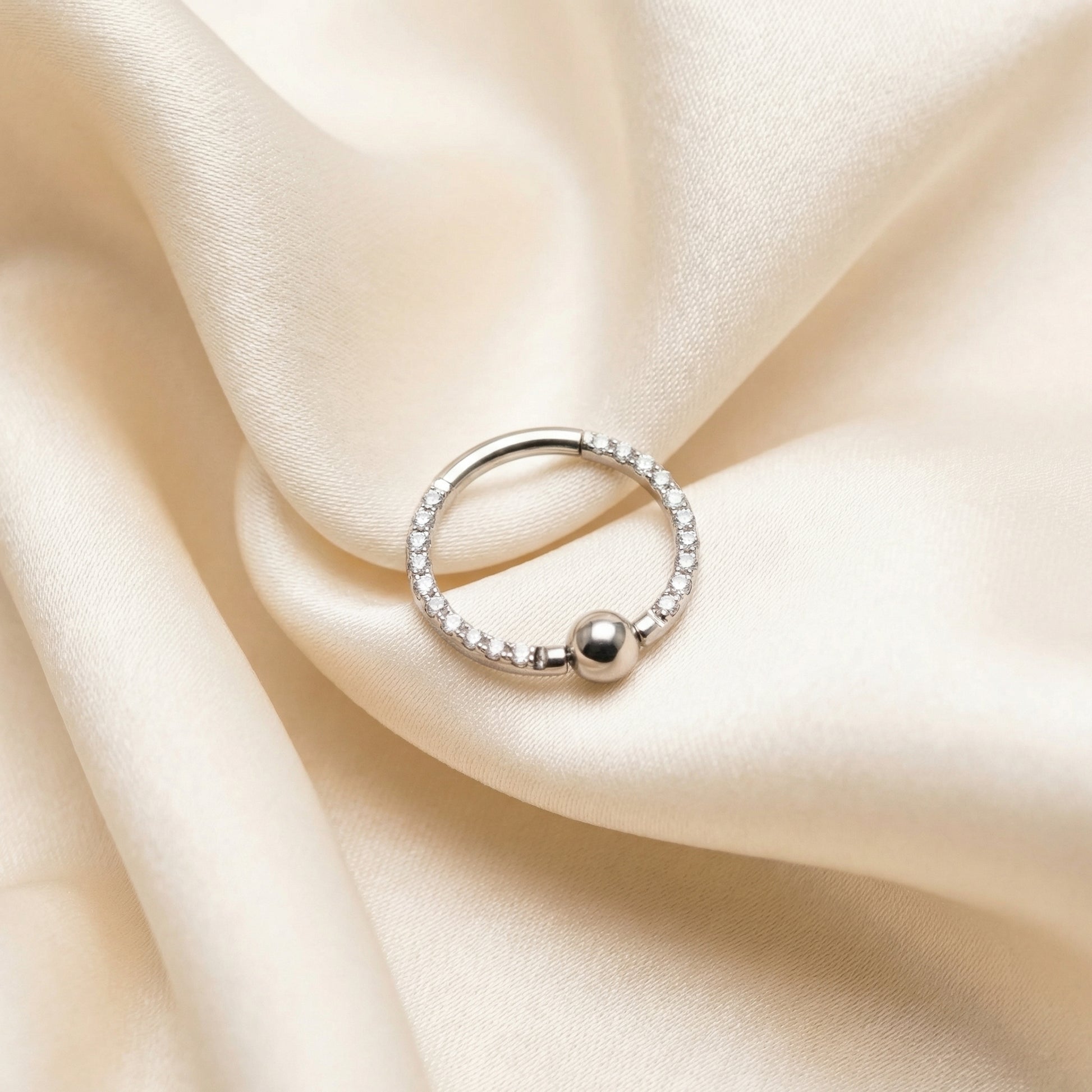 Silver zircon center bead clicker ring nestled cleanly within folded cream satin