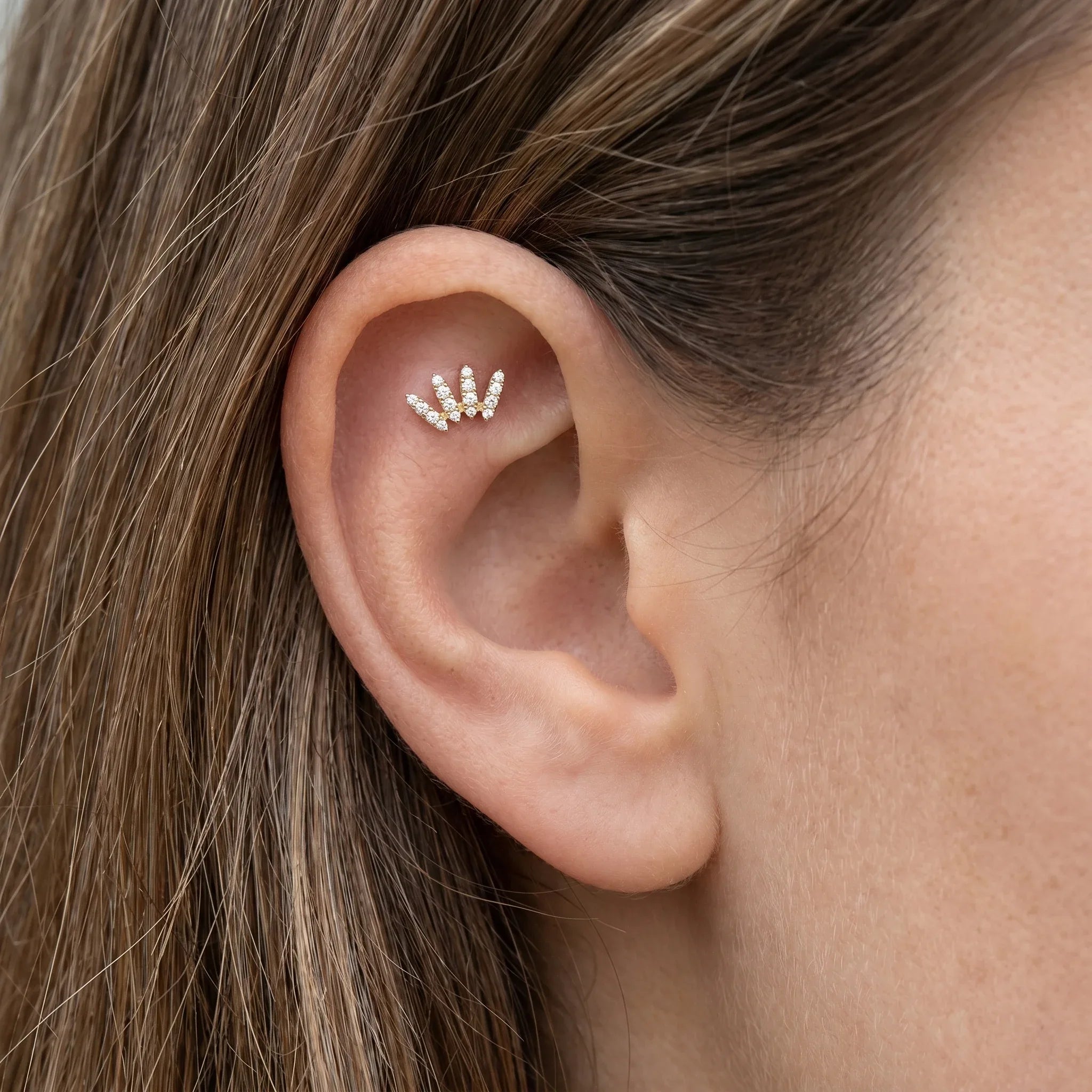 Gold crawler stud worn in a cartilage ear piercing.