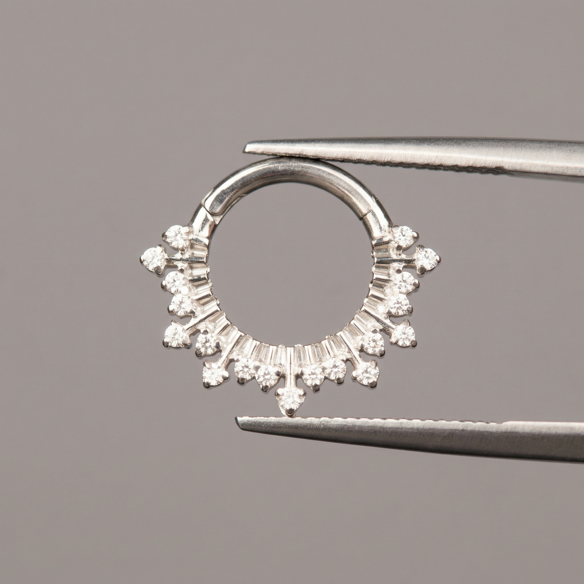Surgical tweezers displaying a silver titanium zircon crown hinged clicker hoop ring.