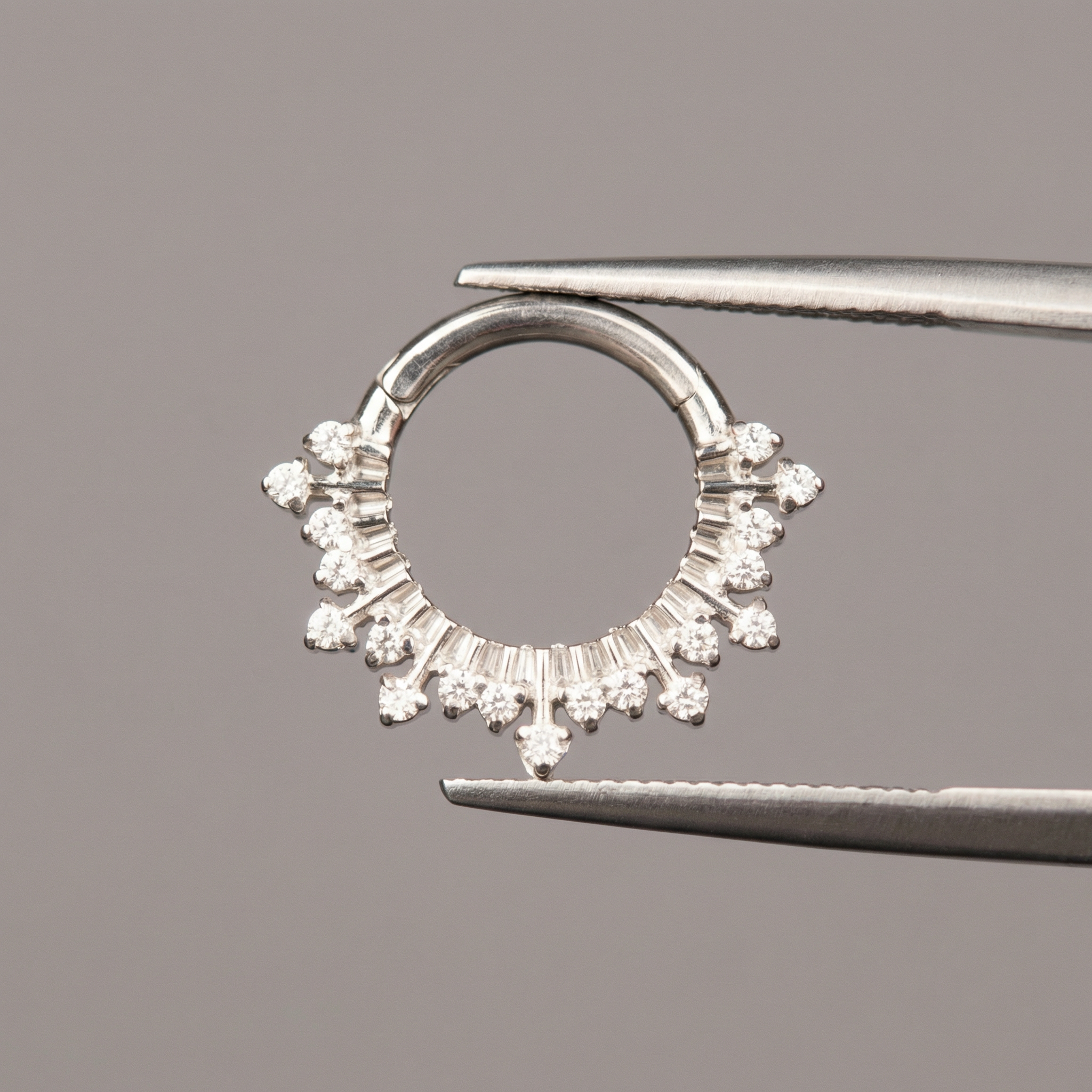 Surgical tweezers displaying a silver titanium zircon crown hinged clicker hoop ring.