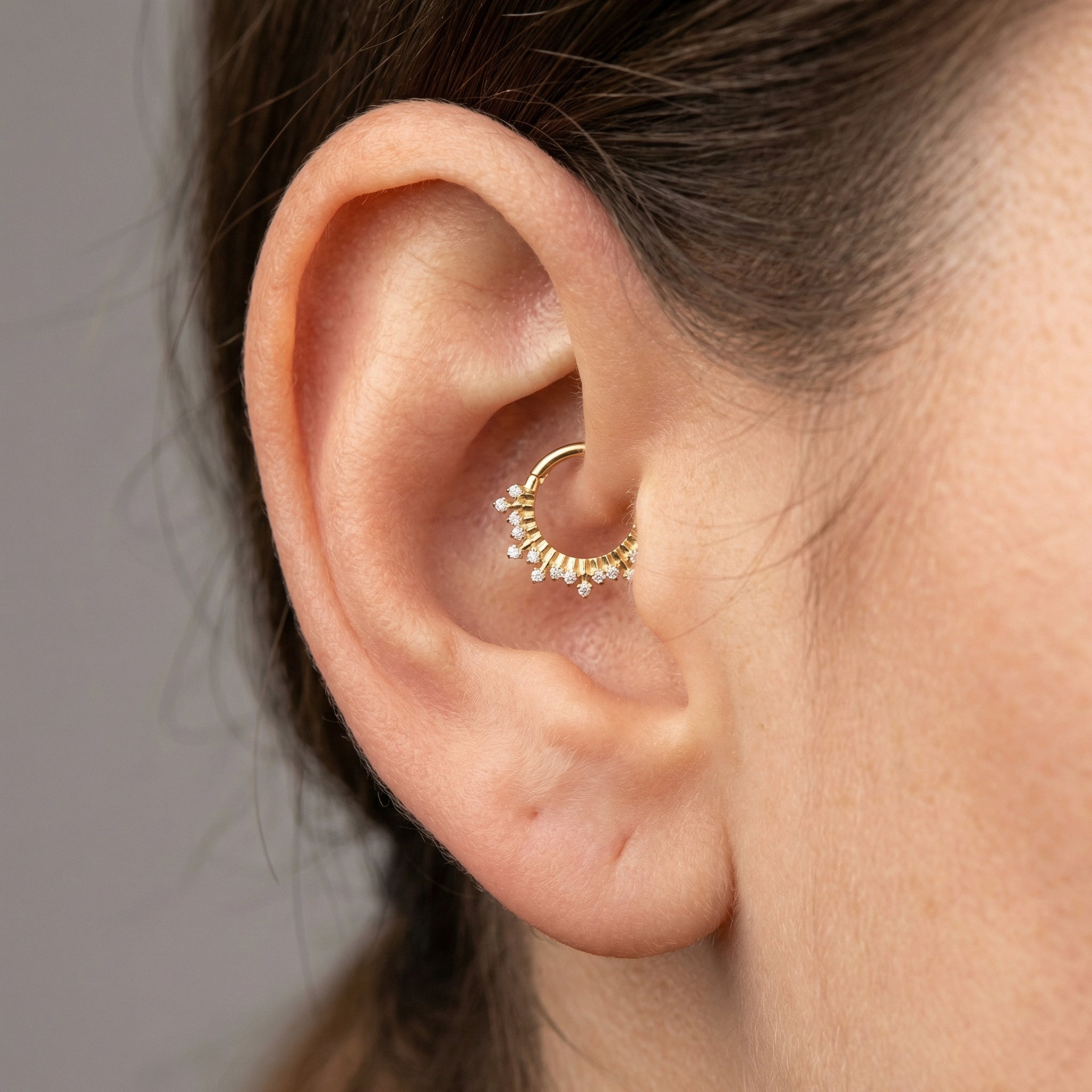 Close-up of a gold zircon crown clicker worn in a model's inner