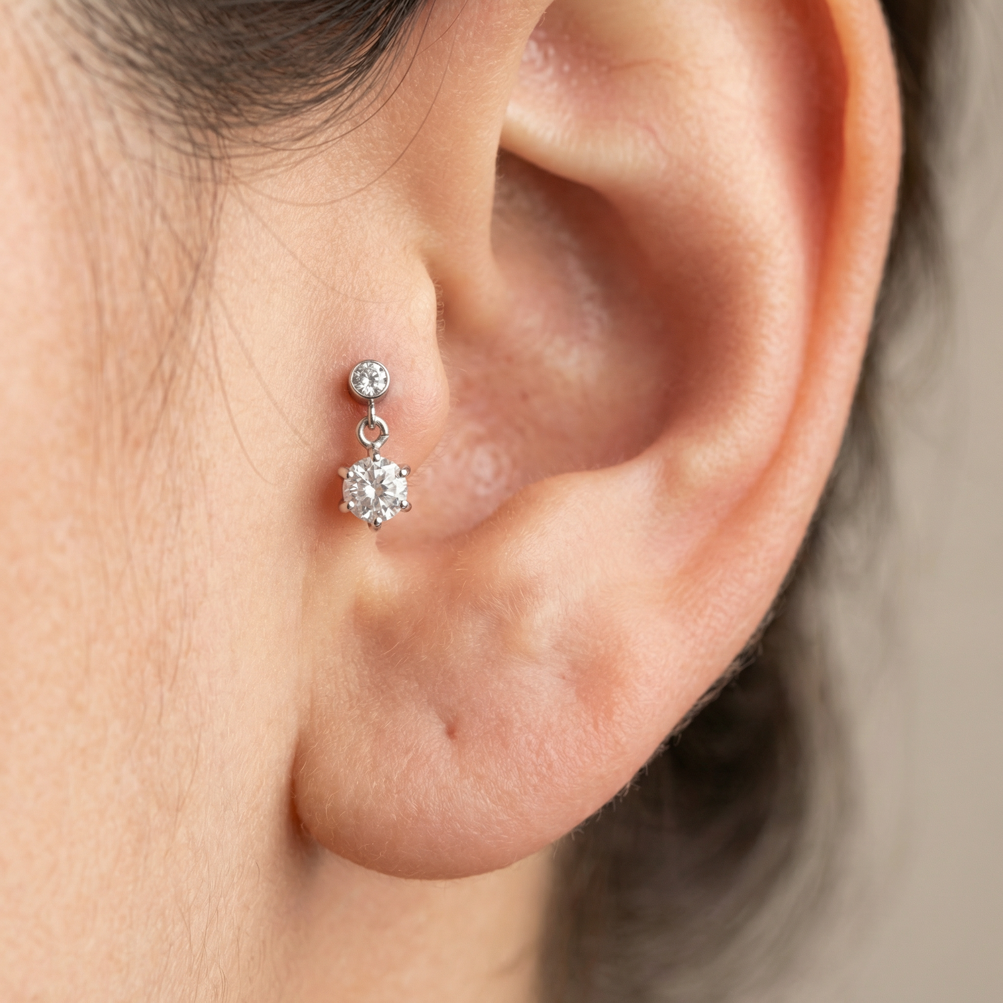 Silver zircon dangle stud styled cleanly in a model's inner cartilage.