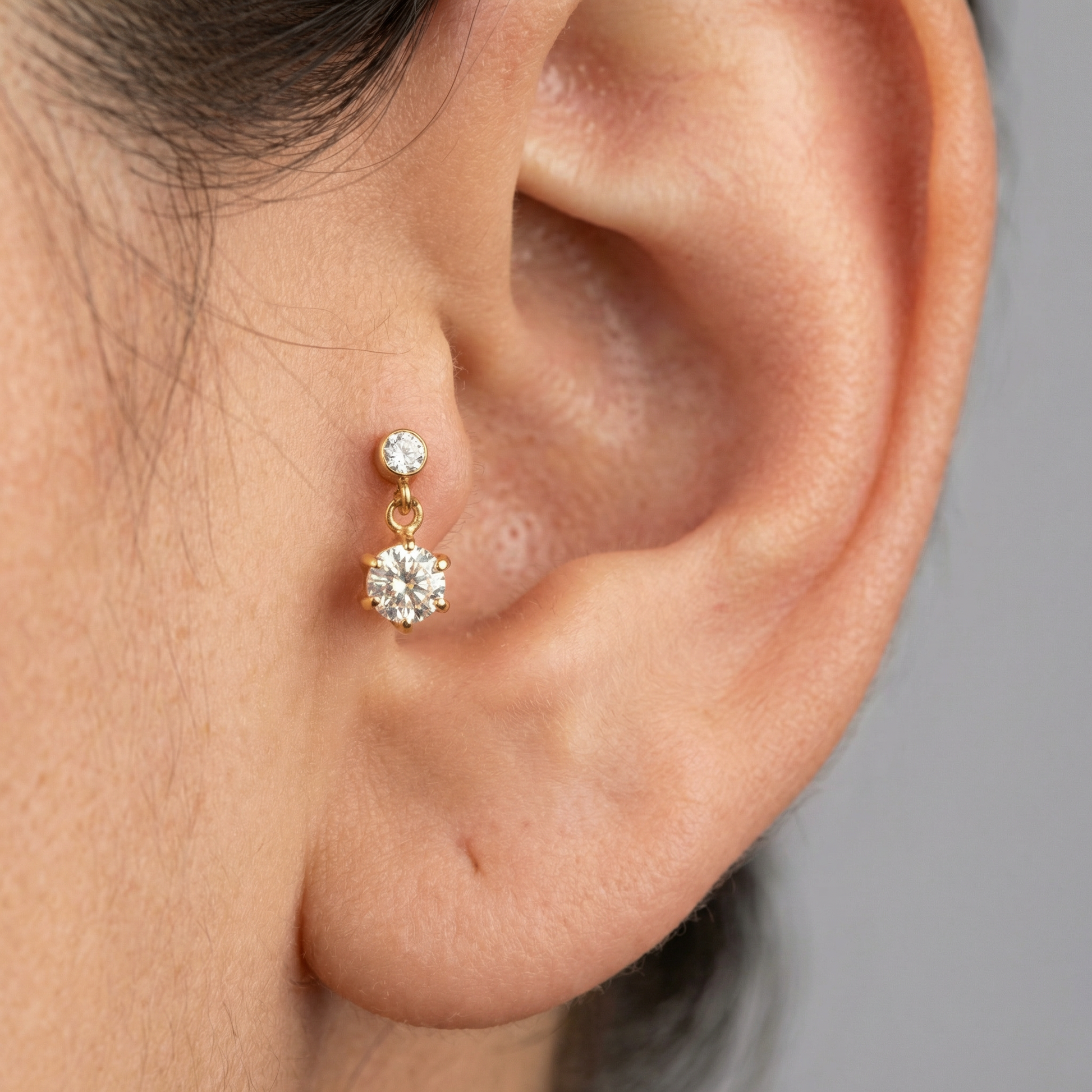 Gold zircon dangle worn securely within a model's piercing.