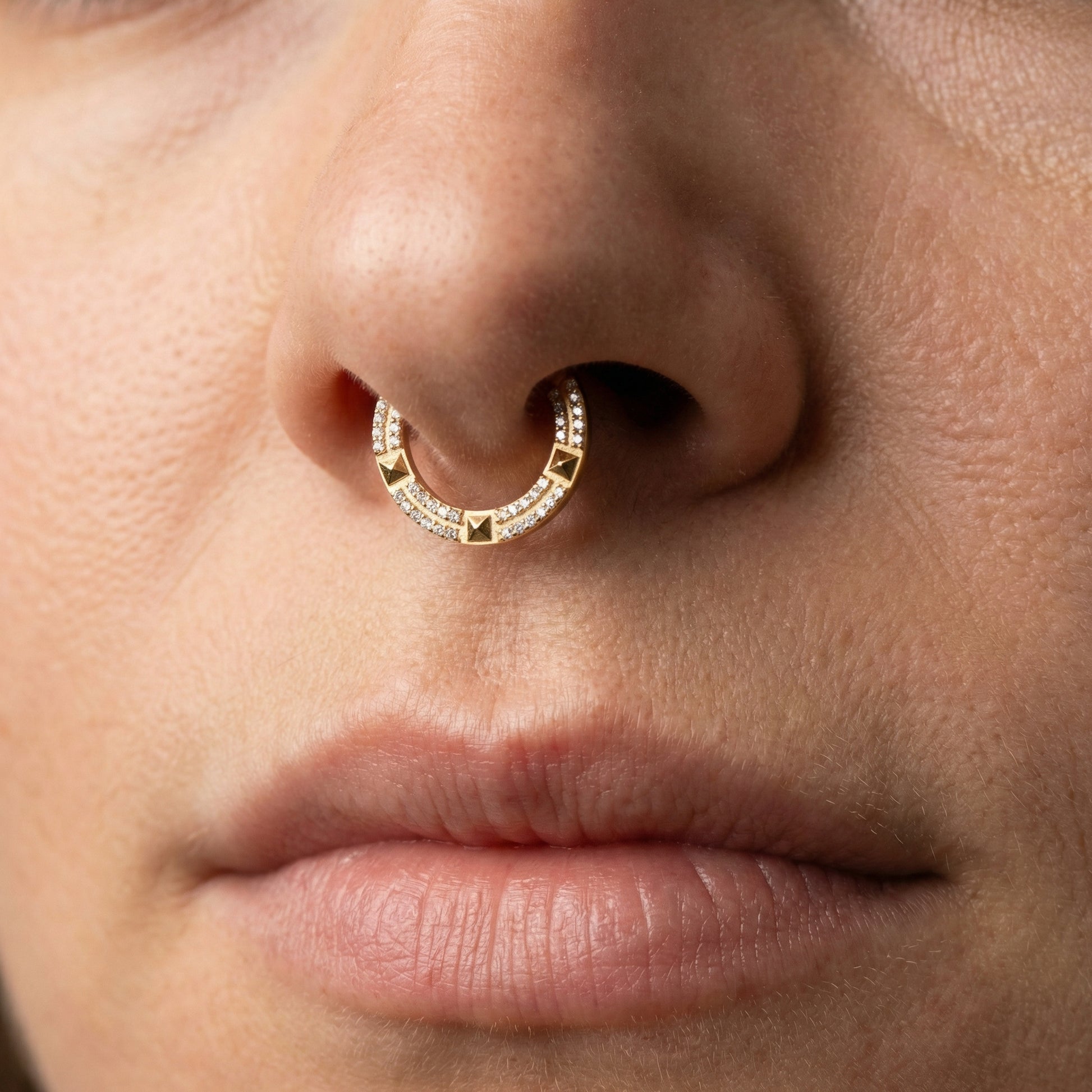 Close-up of a gold geometric zircon clicker worn in a model's piercing.