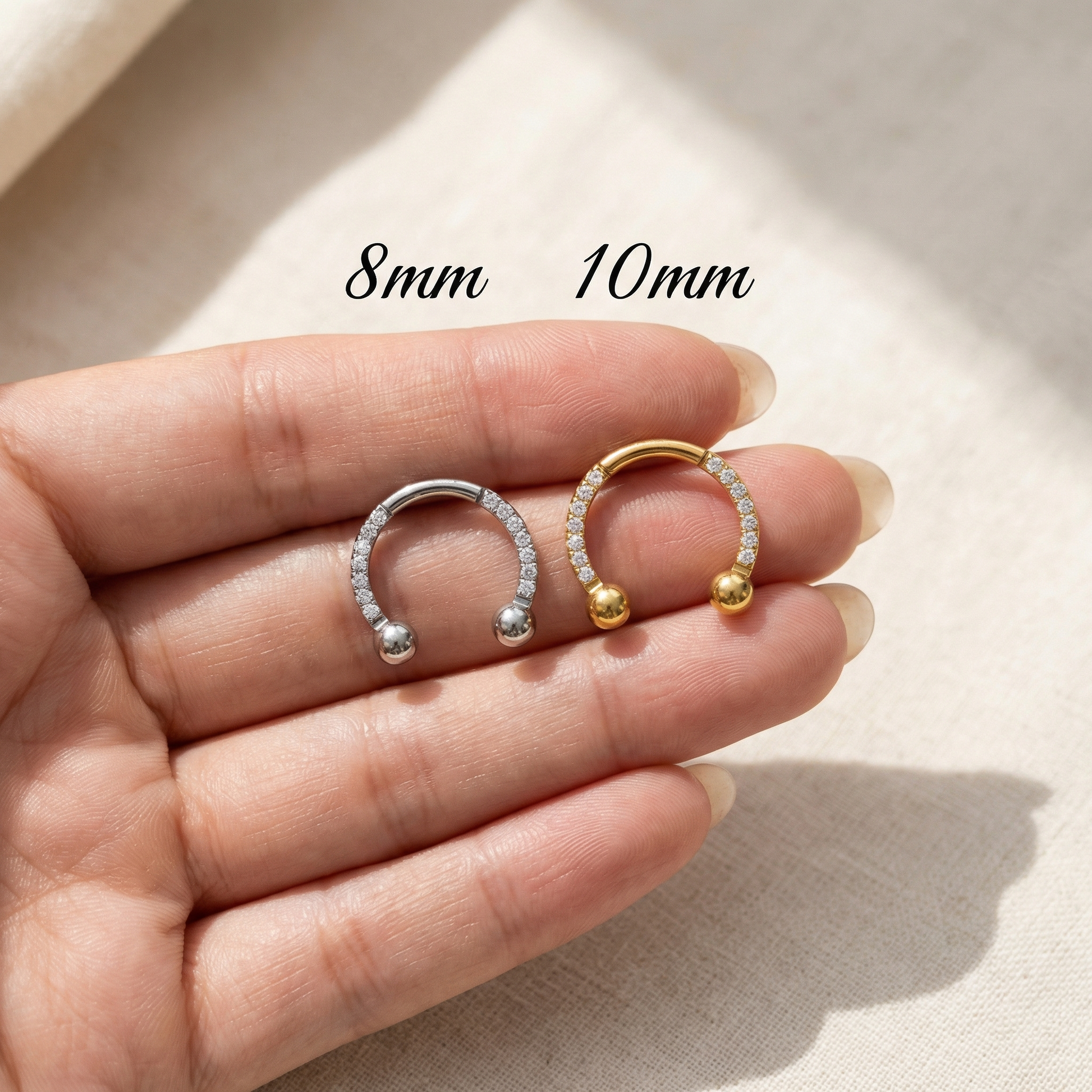 Hand holding 8mm and 10mm silver zircon pave hinged horseshoe clicker rings