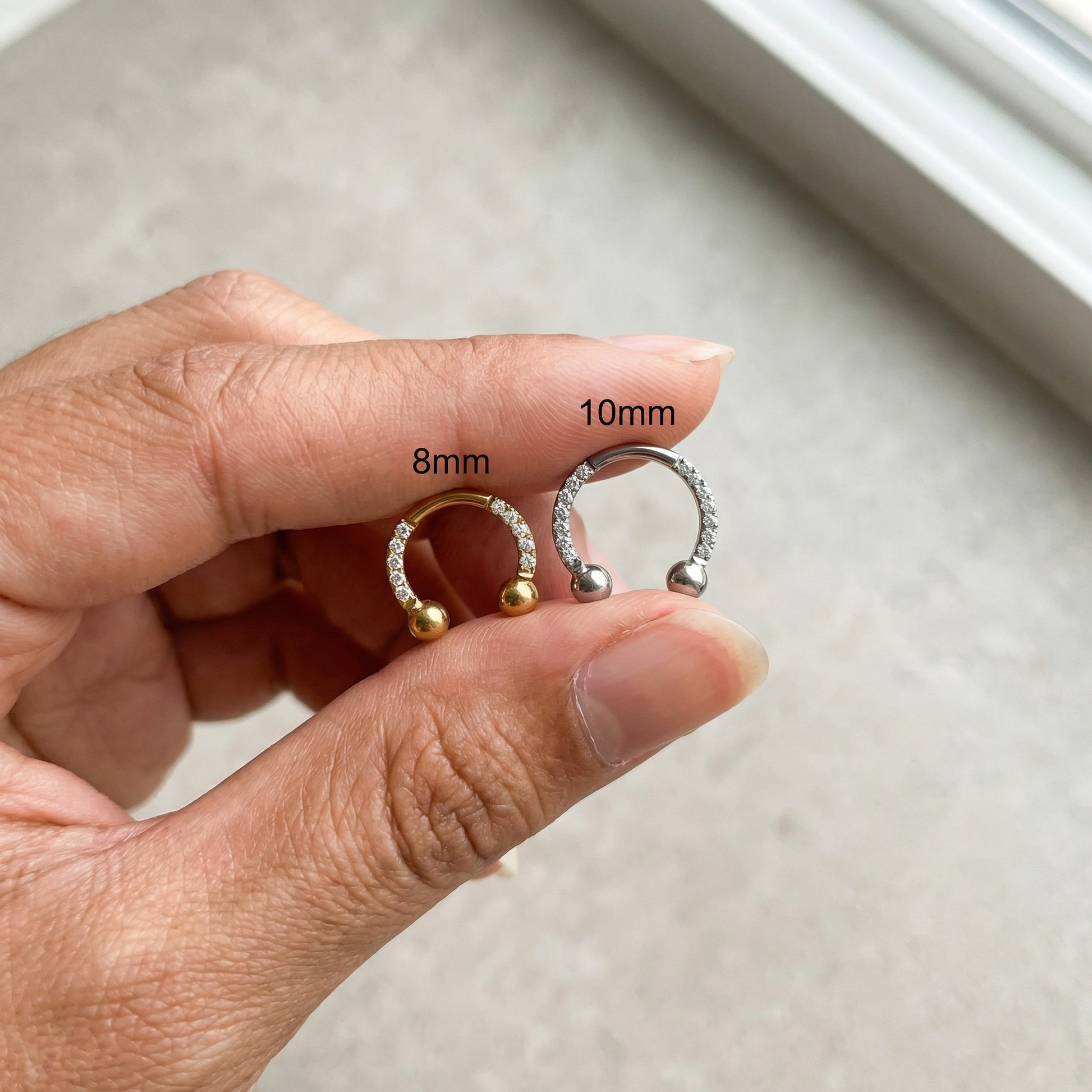 Hand holding 8mm and 10mm gold zircon pave hinged horseshoe clicker rings