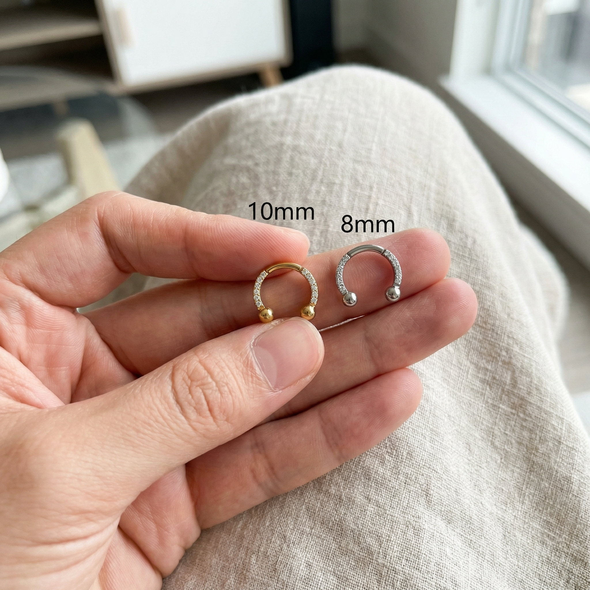 Hand holding 10mm and 8mm silver zircon pave hinged horseshoe clicker rings
