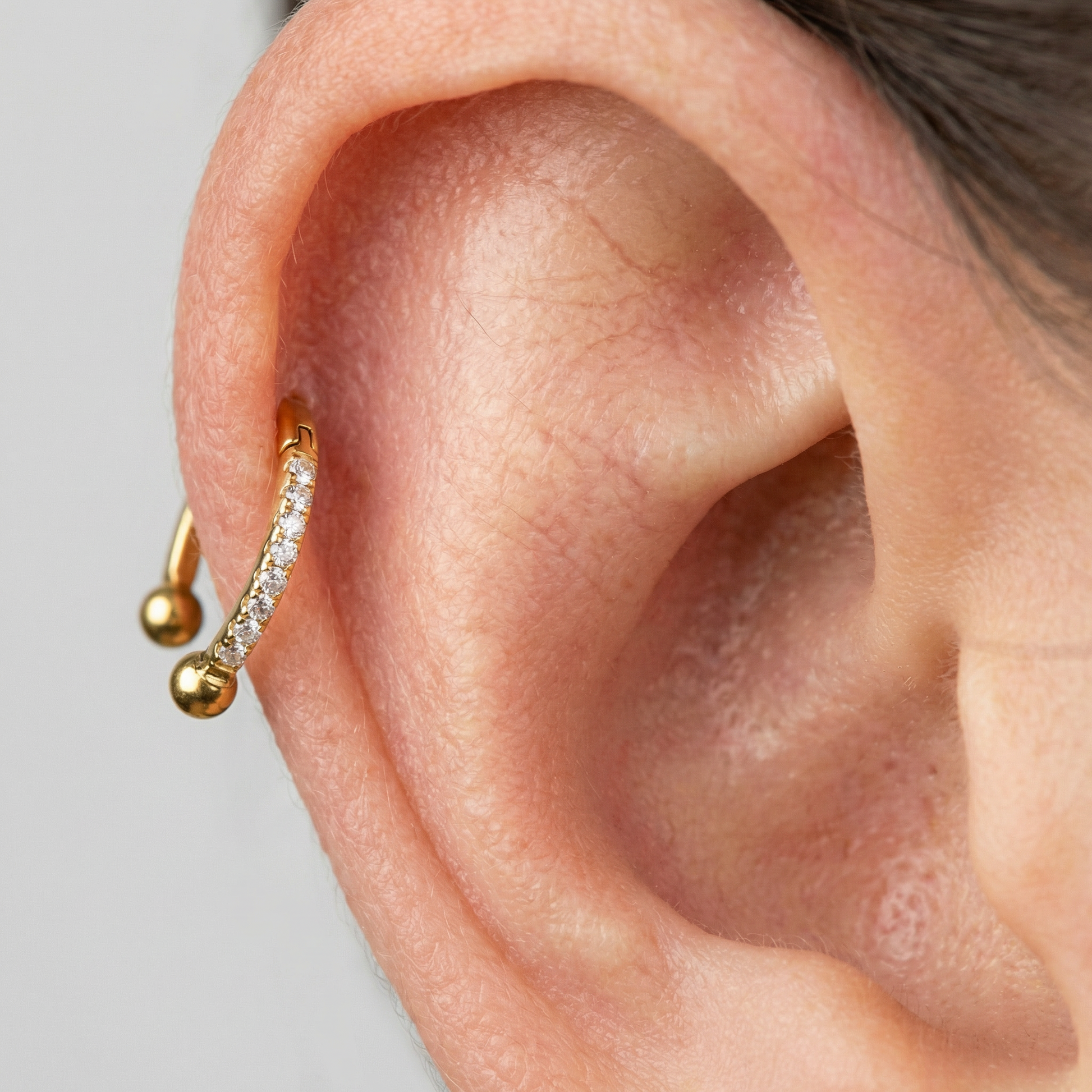 Close-up profile of a gold zircon pave hinged horseshoe clicker ring resting
